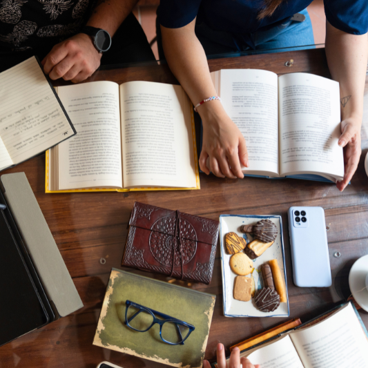Aufnahme in Vogelperspektive von einem Tisch mit aufgeschlagenen Notizbüchern, Kaffee und Keksen