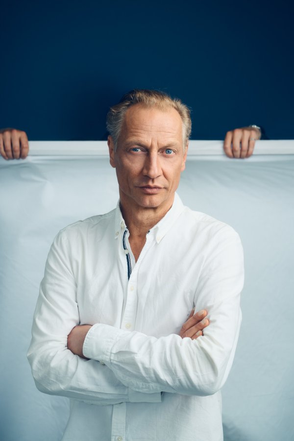 Portrait des Autors Victor Schefé. Er steht in weißem Hemd vor einem blau, weißen Hintergrund.