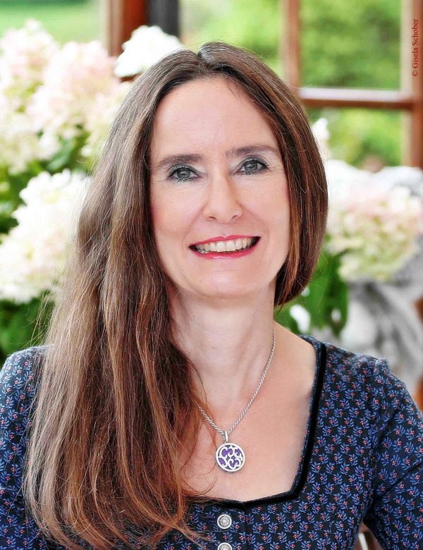 Portrait der Autorin Tanja Kinkel. Sie steht vor weißen Blumen und lächelt.