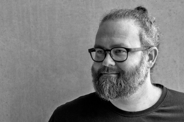 Portrait des Autors Robert Wolfgang Segel. Er trägt ein dunkles T-Shirt und eine schwarze Brille.