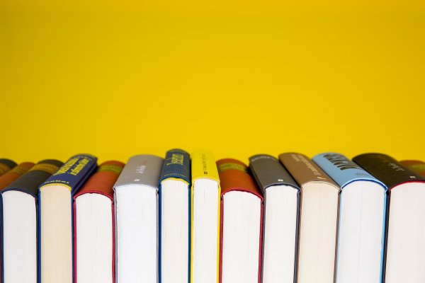 Mehrere Bücher stehen eng nebeneinander mit ihren Buchrücken nach unten vor einem gelben Hintergrund