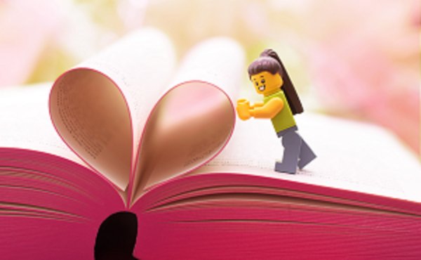 Spielfigur Mädchen steht auf einem Buch bei dem 2 Blätter eine Herzform bilden