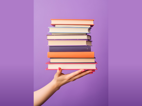 Ein Bücherstapel wird vor einem lila Hintergrund von einer Hand hochgehalten
