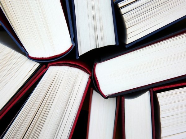 Mehrere Bücher mit dunklem Einband liegen im Kreis angeordnet, sodass ihre aufgeschlagenen Seiten in die Bildmitte zeigen.