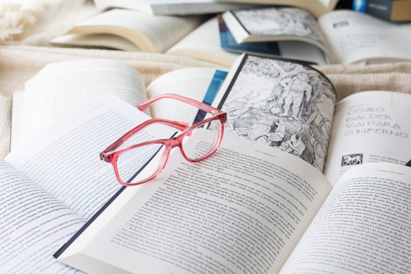 Eine rosa Brille liegt auf einem aufgeschlagenen Buch inmitten mehrerer geöffneter Bücher mit bedruckten Seiten.