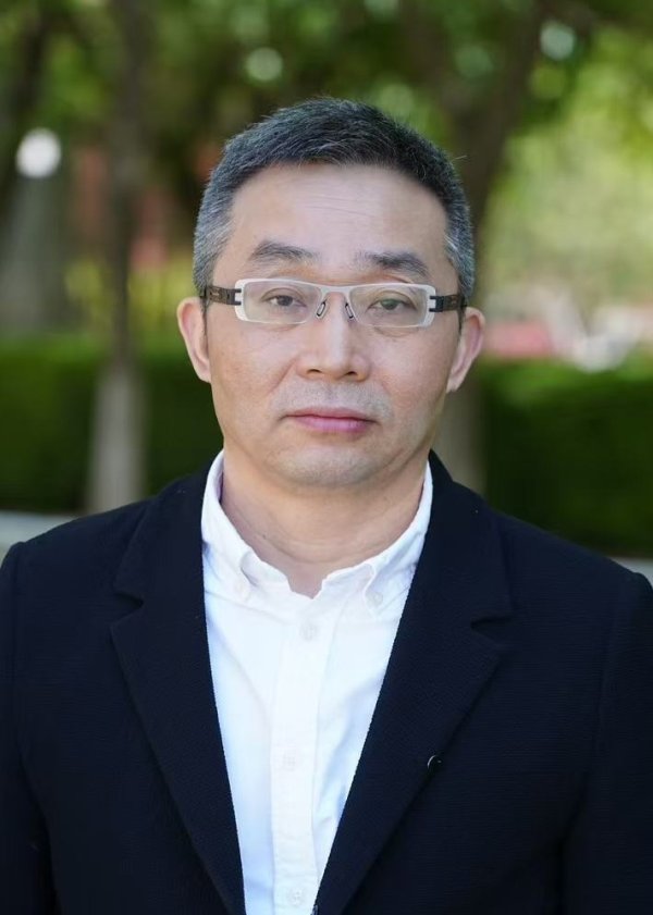 Der Schriftsteller Dong Xi: Porträt einer Person mit Brille, weißem Hemd und dunklem Sakko vor grünem Hintergrund im Freien.