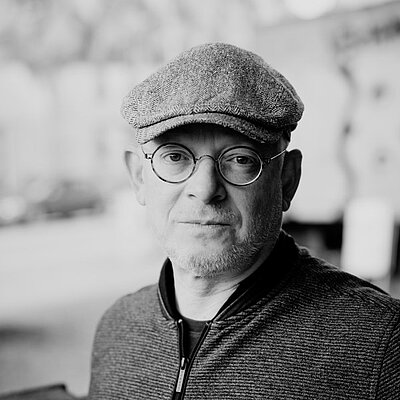 Portrait des Autors Timur Vermes in schwarz-weiß. Er trägt eine Kappe und eine runde Brille.