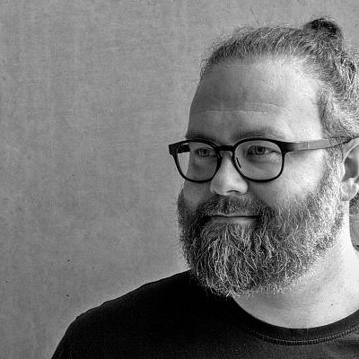 Portrait des Autors Robert Wolfgang Segel. Er trägt ein dunkles T-Shirt und eine schwarze Brille.