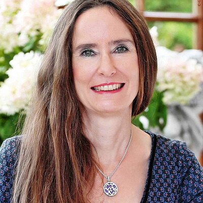 Portrait der Autorin Tanja Kinkel. Sie steht vor weißen Blumen und lächelt.