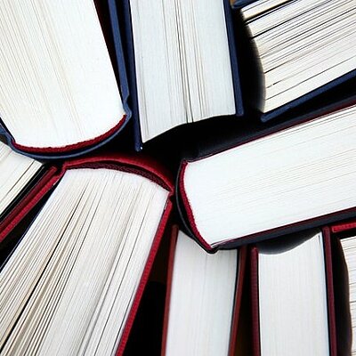 Mehrere Bücher mit dunklem Einband liegen im Kreis angeordnet, sodass ihre aufgeschlagenen Seiten in die Bildmitte zeigen.