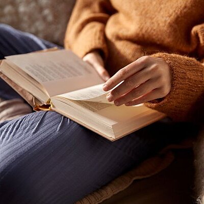 woman in warm sweater reading book at home on a sofa