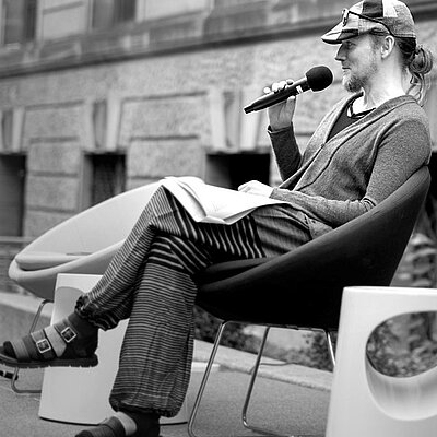 Experte Christian Schloyer sitzt auf einem Designerstuhl und redet in ein Mikrofon.