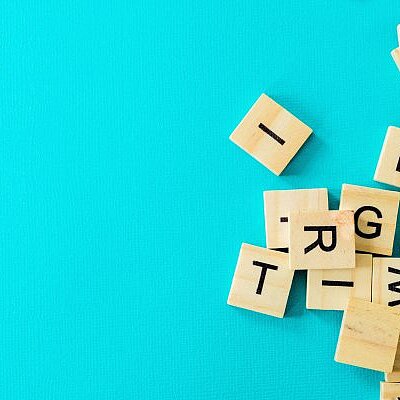 Durcheinander liegende Holzbuchstaben-Spielsteine auf türkisfarbenem Hintergrund.