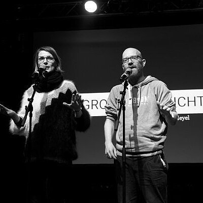 Pauline Füg und Tobias Heyel auf der Bühne bei einem vergangenen Poetry-Slam. Bild in schwarz-weiß.