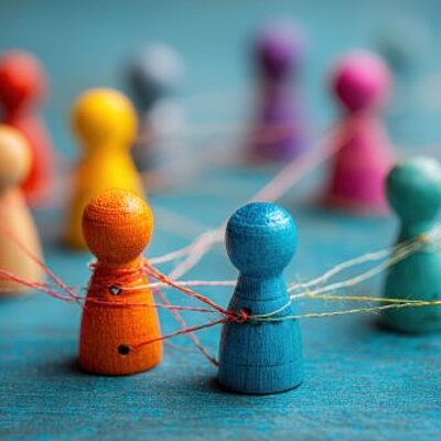 Bunt bemalte Holzfiguren sind durch Fäden netzwerkartig miteinander verbunden.