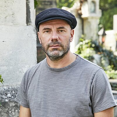 Portrait des Autors Daniel Wisser. Er steht im Freien und trägt eine schwarze Kappe.